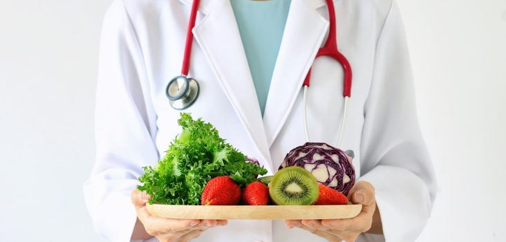 Arzt hält einen Teller mit Obst und Gemüse in der Hand